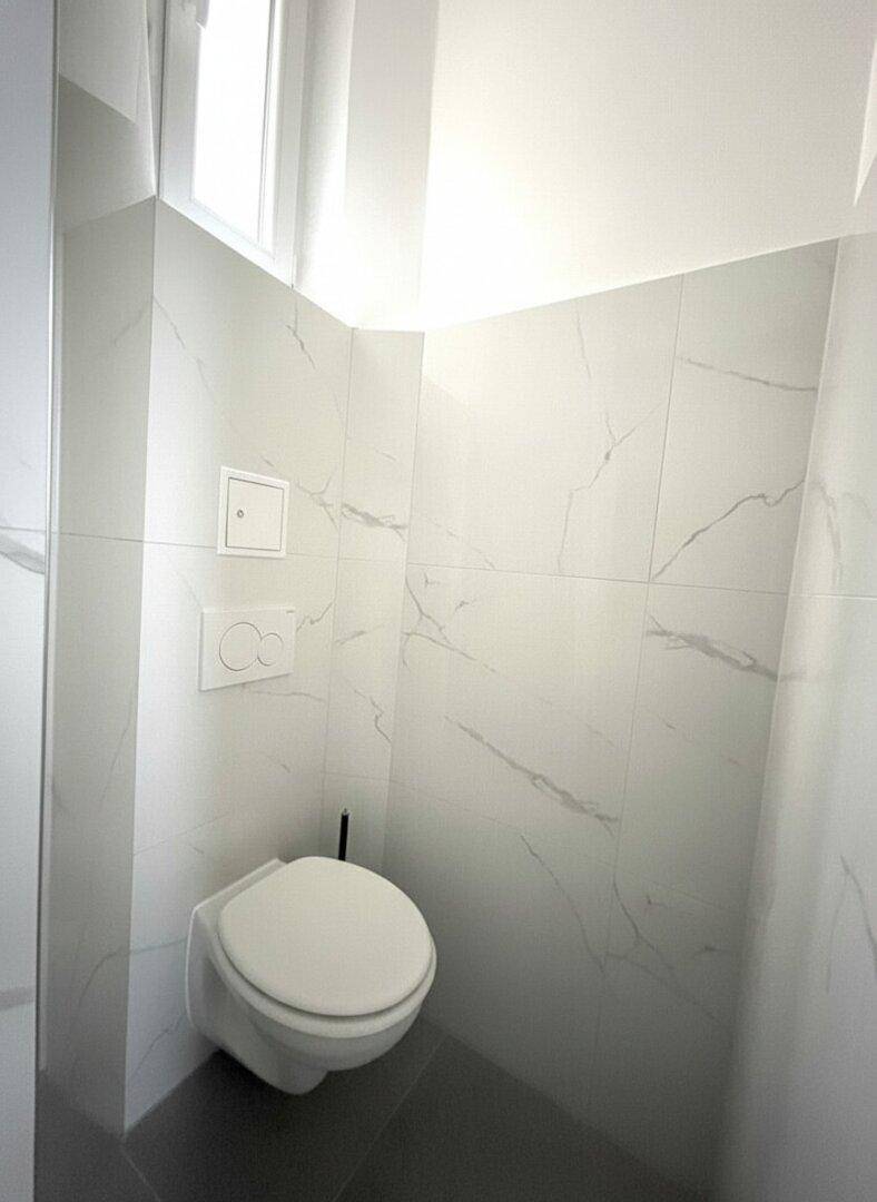 Separates WC mit wandhängender Toilette und modernen weißen Marmorfliesen.