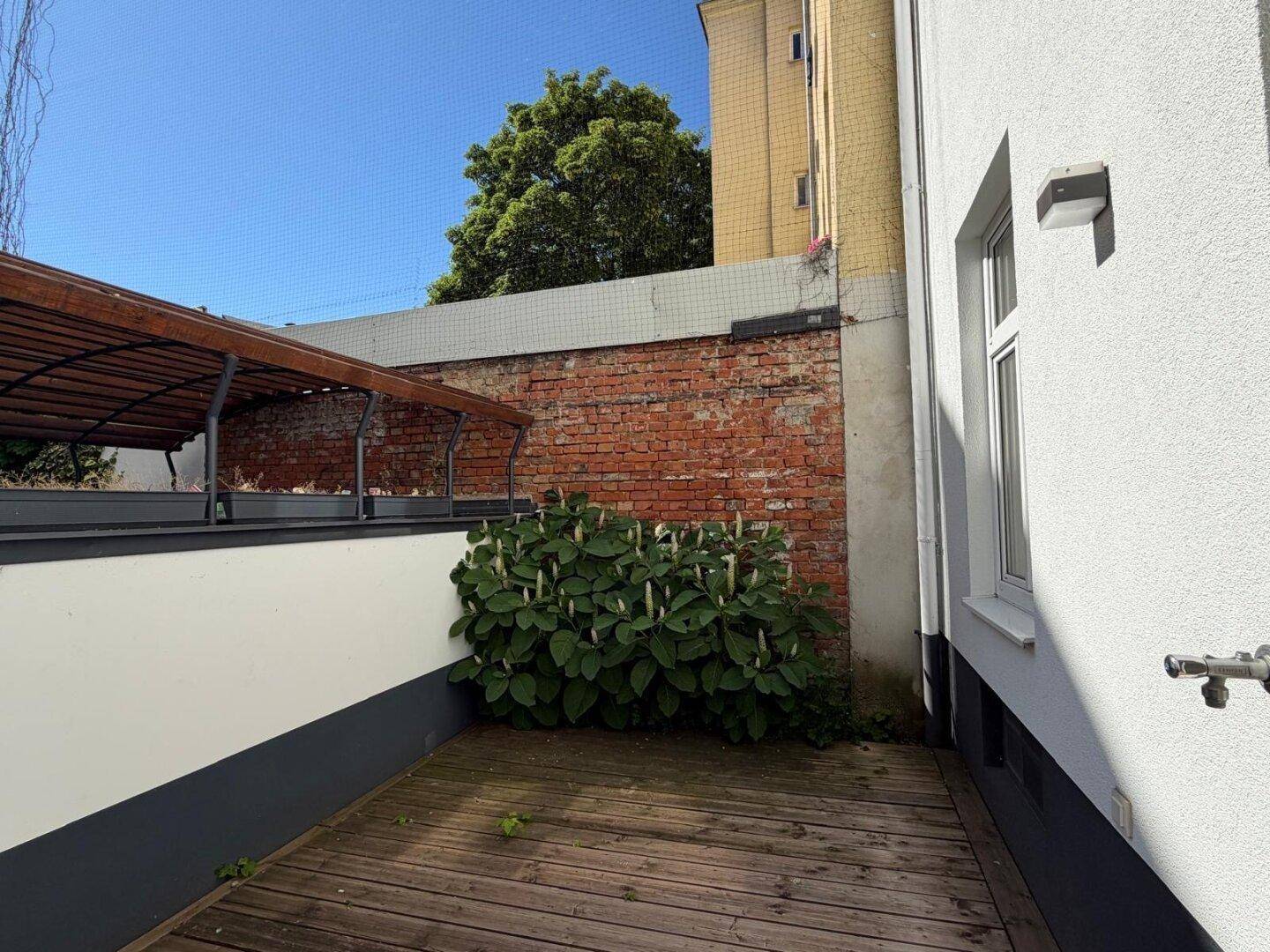 Helle Terrasse mit Holzplankenboden, umgeben von einer Ziegelwand und Grünflächen.