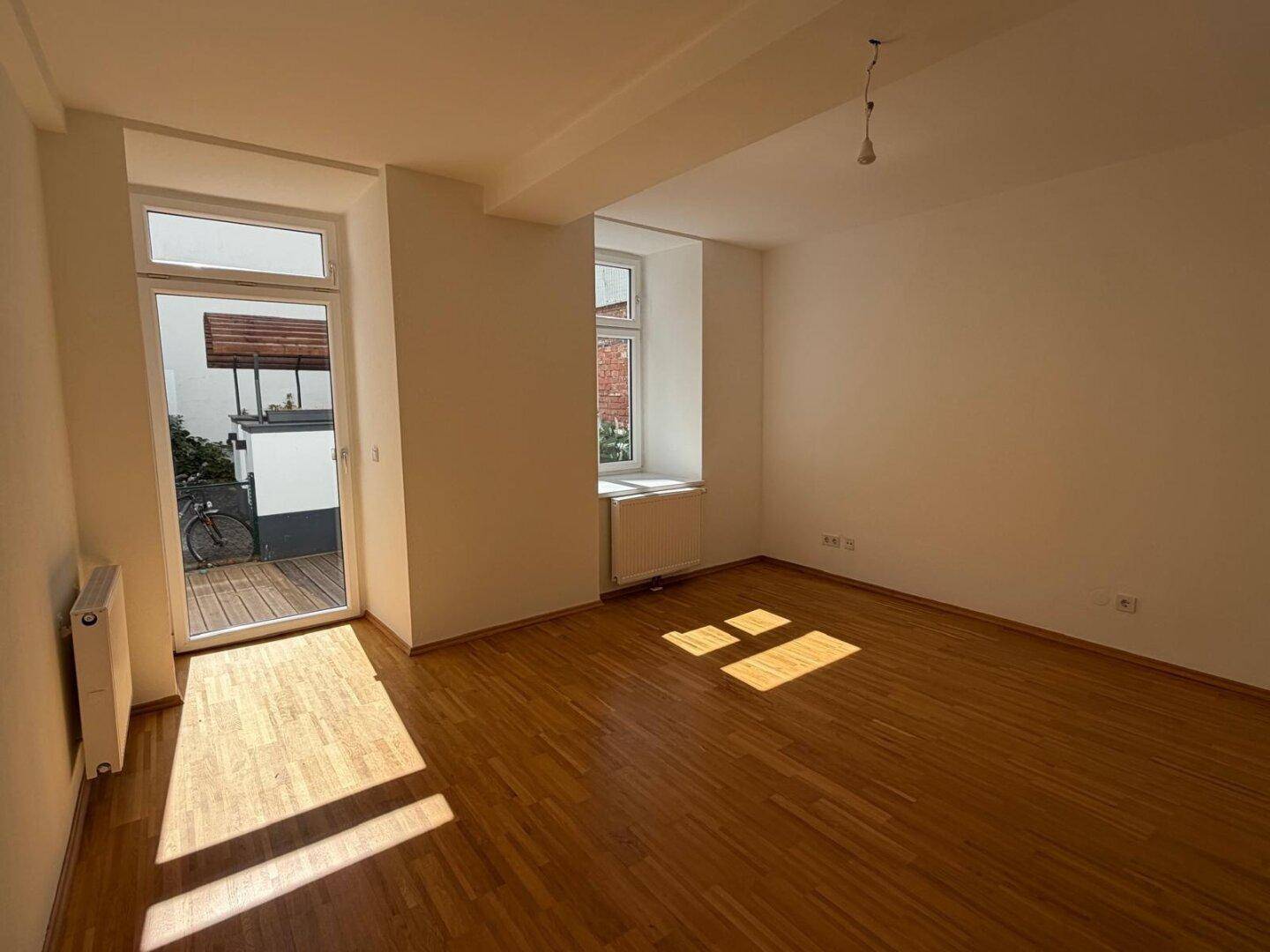 Lichtdurchflutetes Wohnzimmer mit Holzfußboden, großen Fenstern und direktem Zugang zur Terrasse.