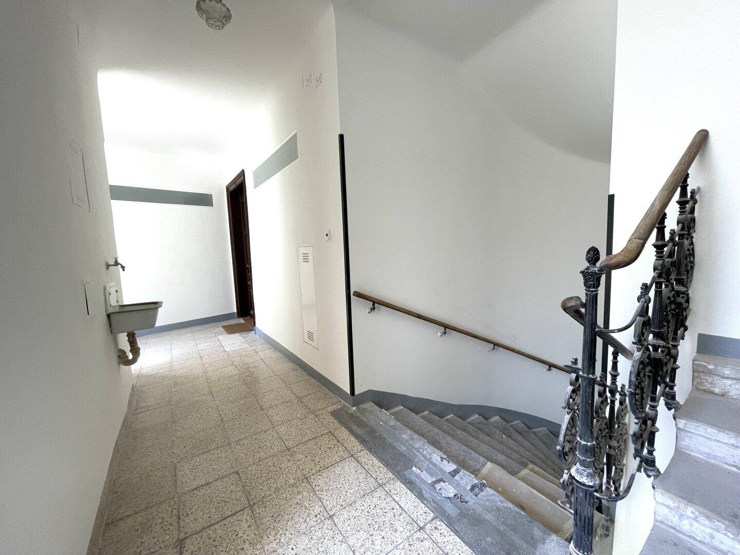 Treppenhaus in einem Mehrfamilienhaus mit gefliestem Boden und einem Waschbecken im Eingangsbereich.