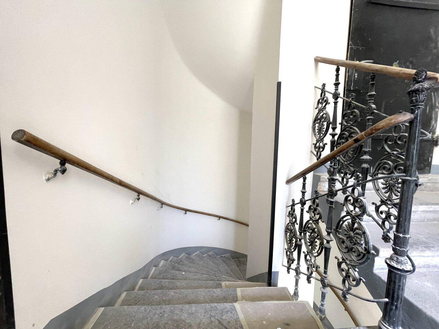Historisches Treppenhaus mit kunstvollem schmiedeeisernem Geländer und Holzhandlauf.