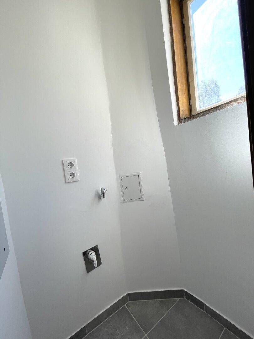 Praktischer Bereich mit Anschlüssen für Waschmaschine und einem Fenster, ideal als Hauswirtschaftsraum.