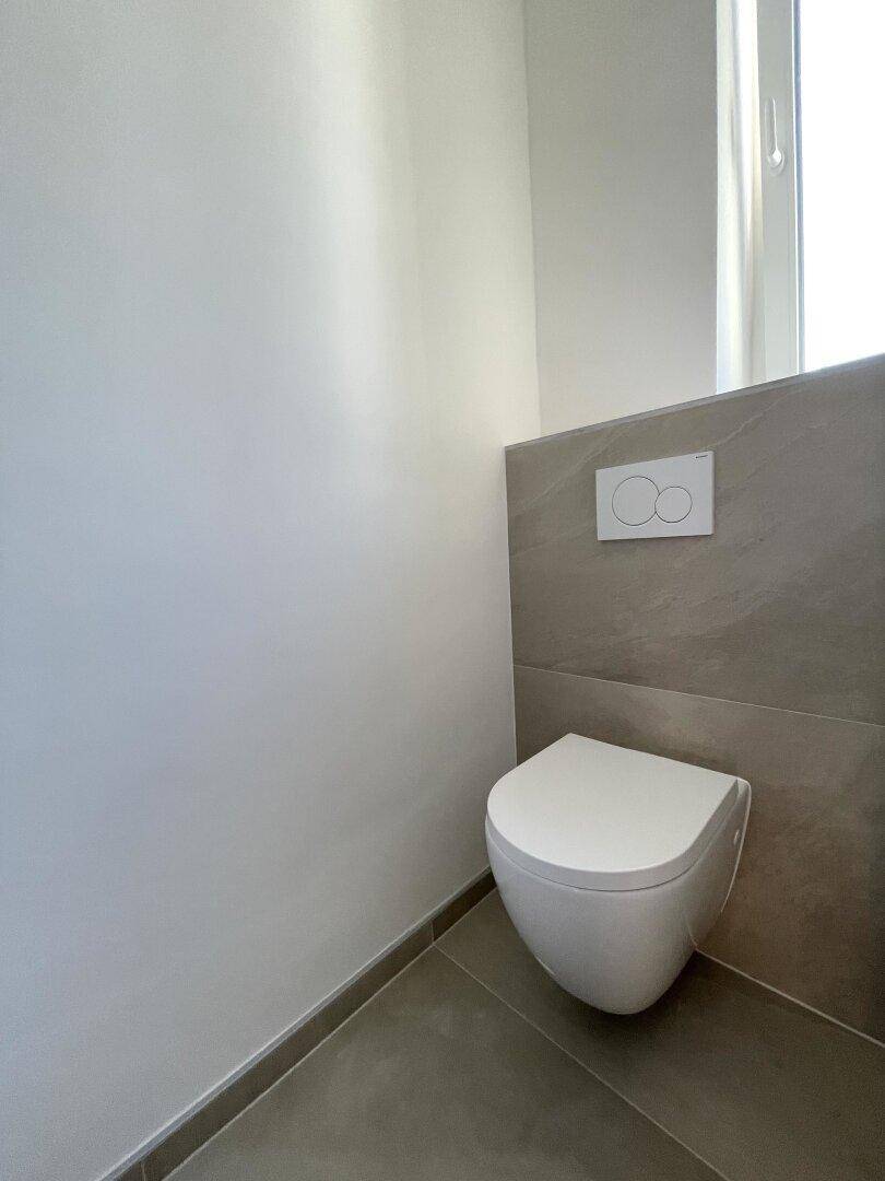 Modernes Wand-WC mit integrierter Spülung und hellen Fliesen im unteren Bereich.