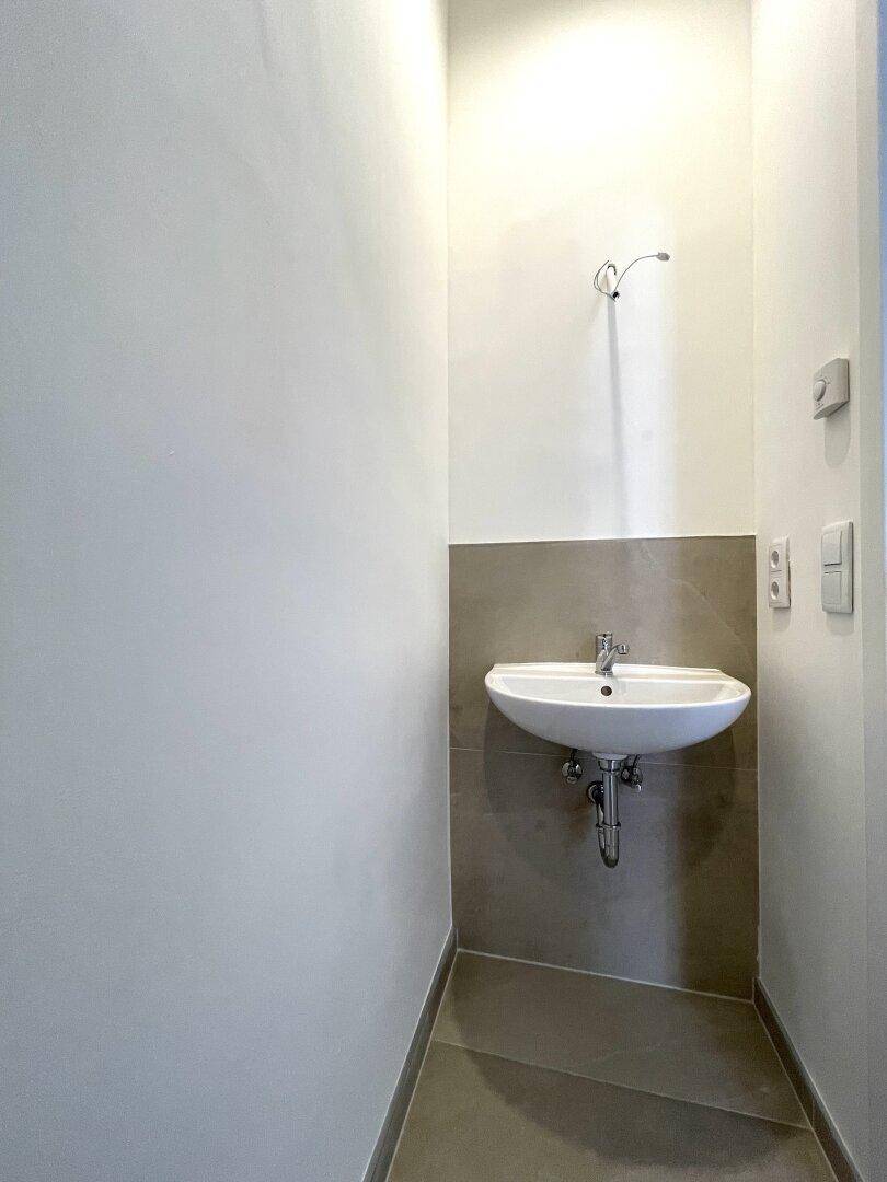Kleines, modernes WC mit Waschbecken und hellen Fliesen an der Wand.