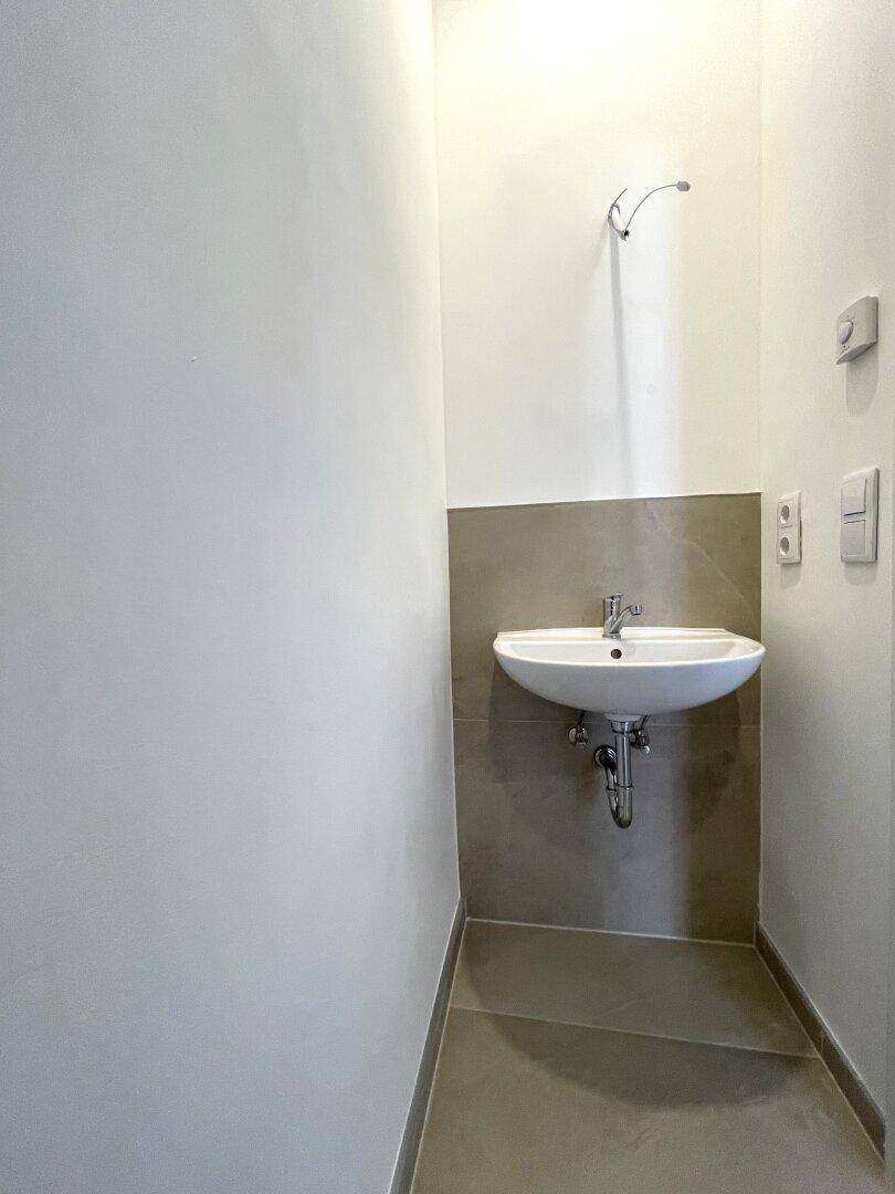 Kleines, modernes WC mit Waschbecken und hellen Fliesen an der Wand.