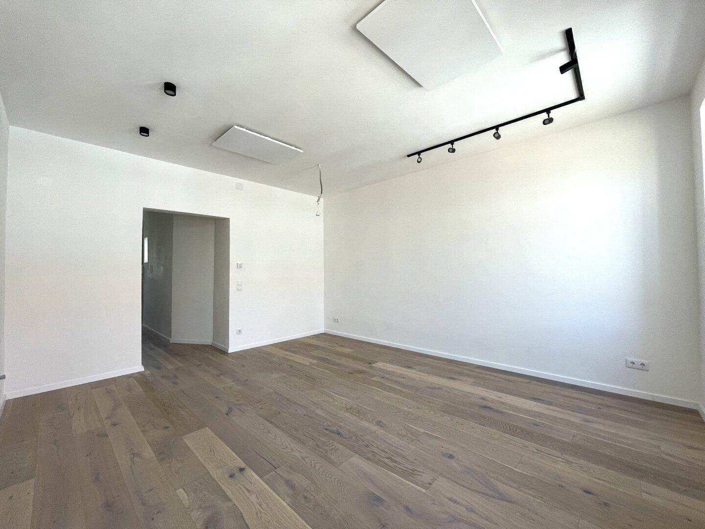Geräumiges, unmöbliertes Zimmer mit hellem Holzfußboden und Zugang zu einem weiteren Raum.
