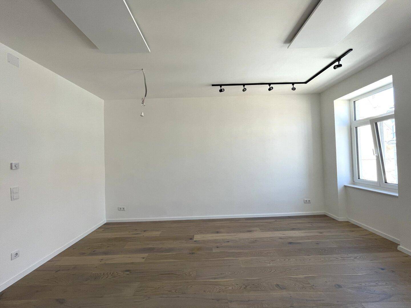 Heller Raum mit modernem Holzfußboden, weißen Wänden und einem großen Fenster für viel Tageslicht.