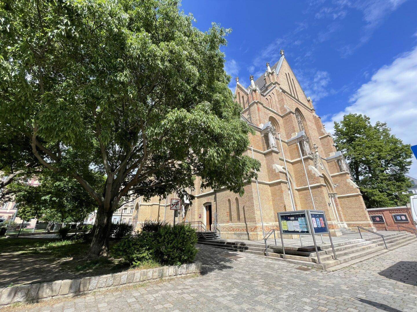 Historische Kirche mit beeindruckender Architektur und einem großen Baum im Vordergrund an einem sonnigen Tag.