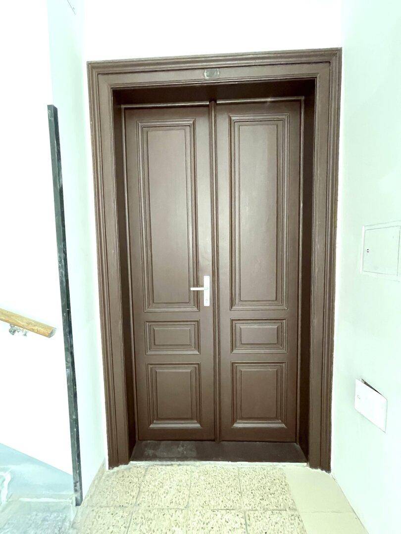 Große, braune Eingangstür mit zwei Flügeln in einem Flur mit Fliesenboden.