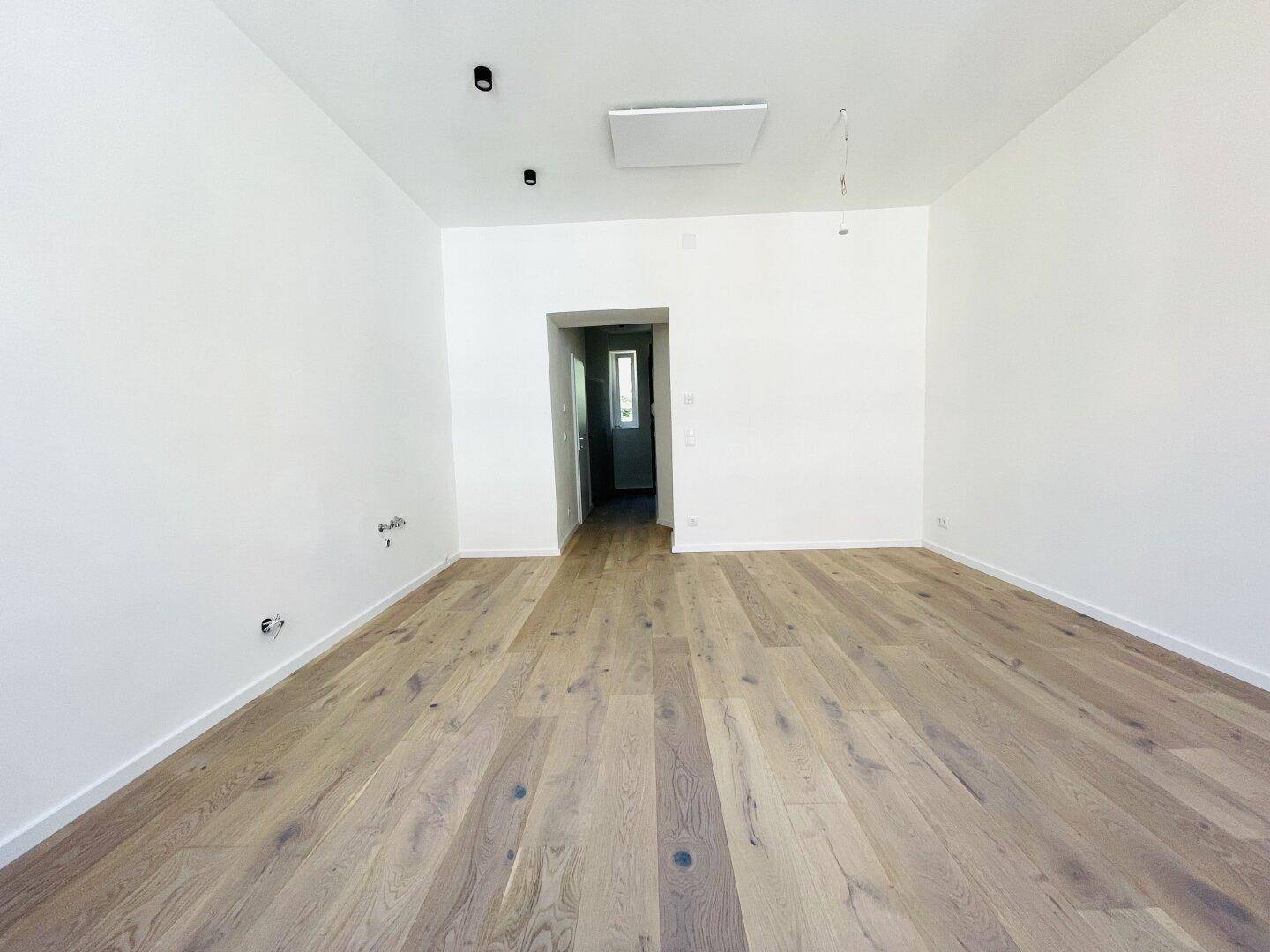 Geräumiges, leeres Zimmer mit Parkettboden und Blick in einen Flur.