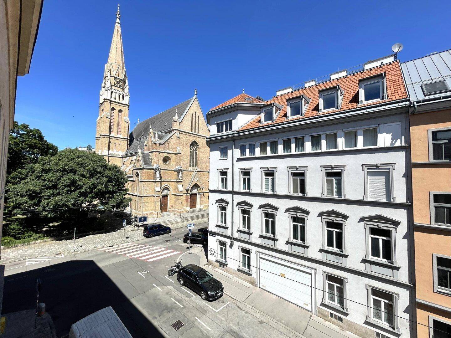 Stadtansicht mit einer historischen Kirche und umliegenden Gebäuden unter blauem Himmel.