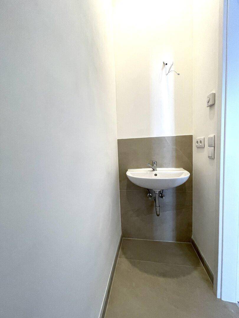 Kleines Waschbecken in einem Raum mit grauen Fliesen und weißen Wänden.