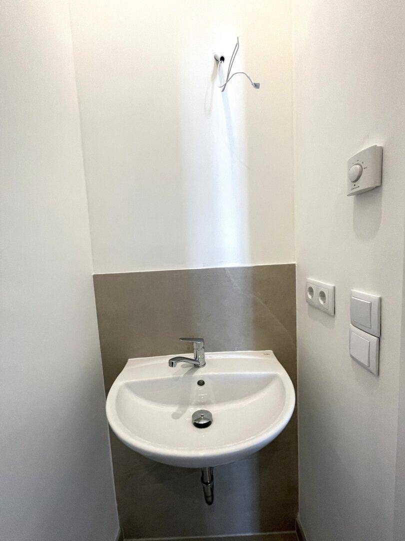 Modernes Waschbecken in einem kleinen Raum mit Fliesen und Steckdosen.