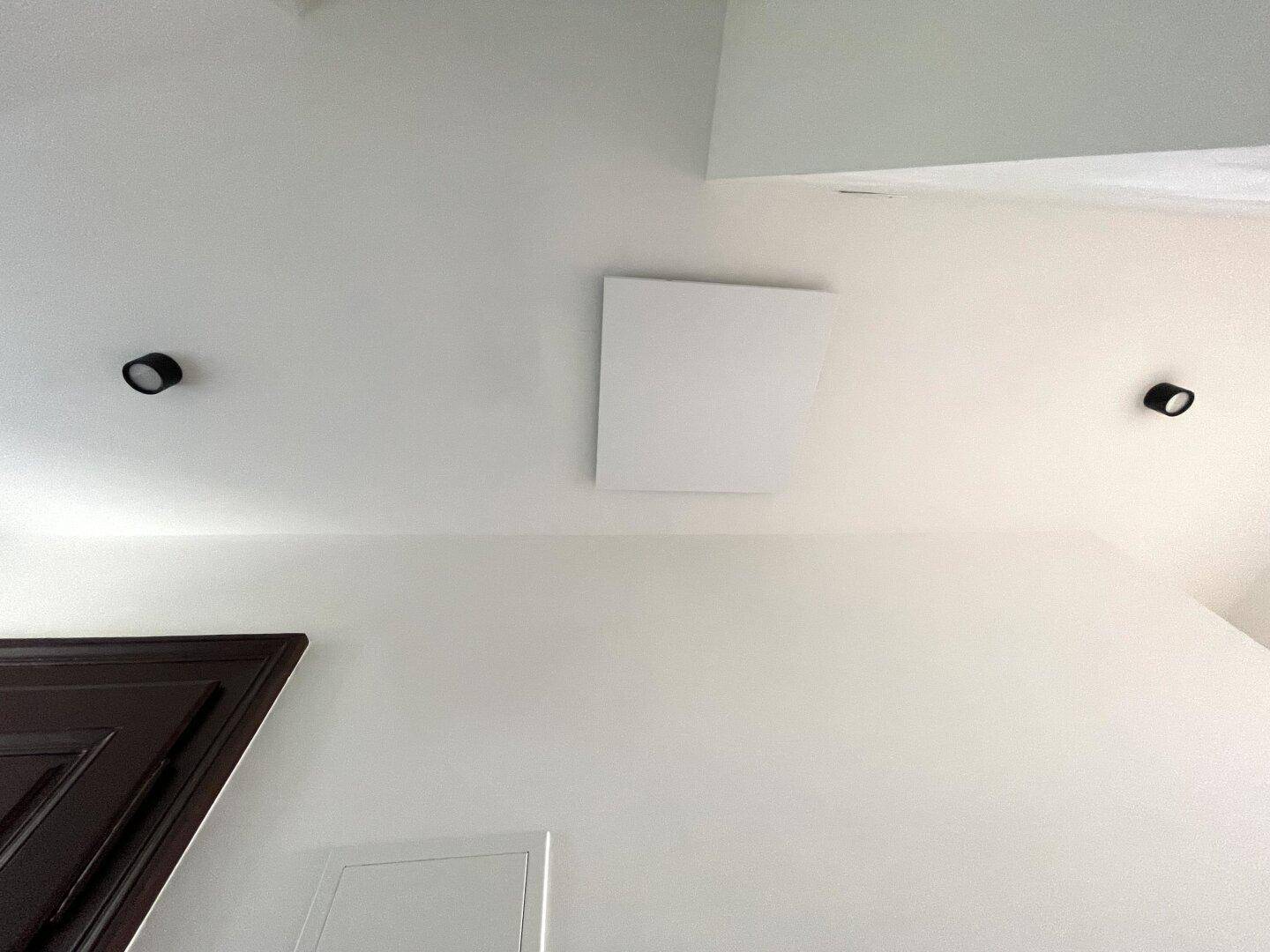 Weiße Decke mit modernen Einbaustrahlern und einem rechteckigen Deckenlicht.
