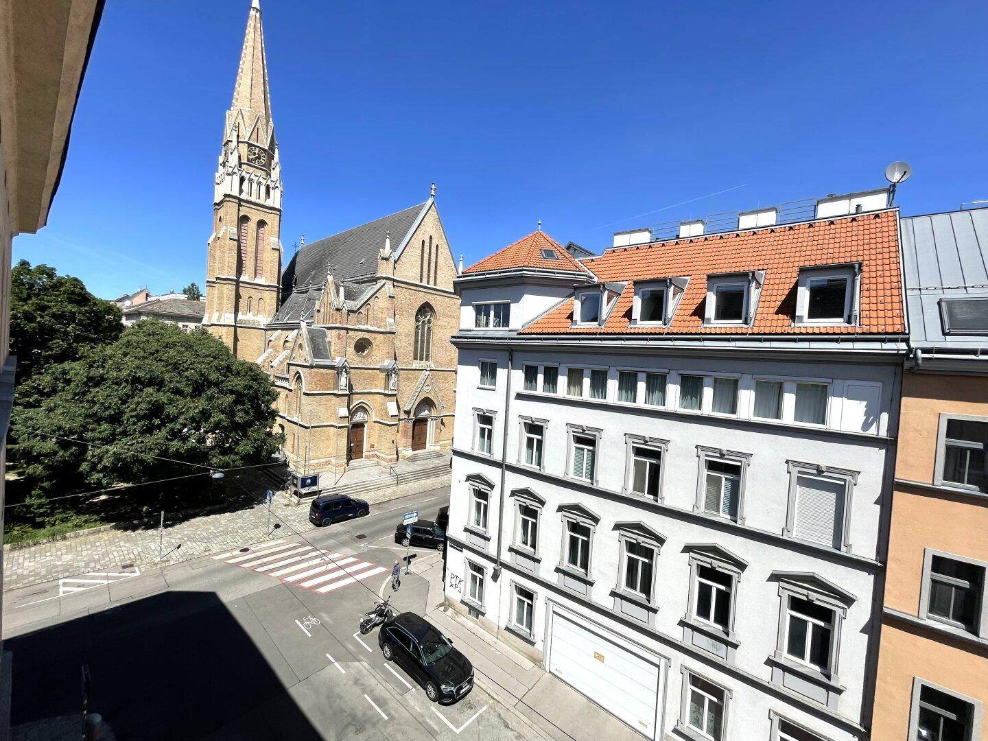 Stadtansicht mit einer historischen Kirche und umliegenden Gebäuden unter blauem Himmel.