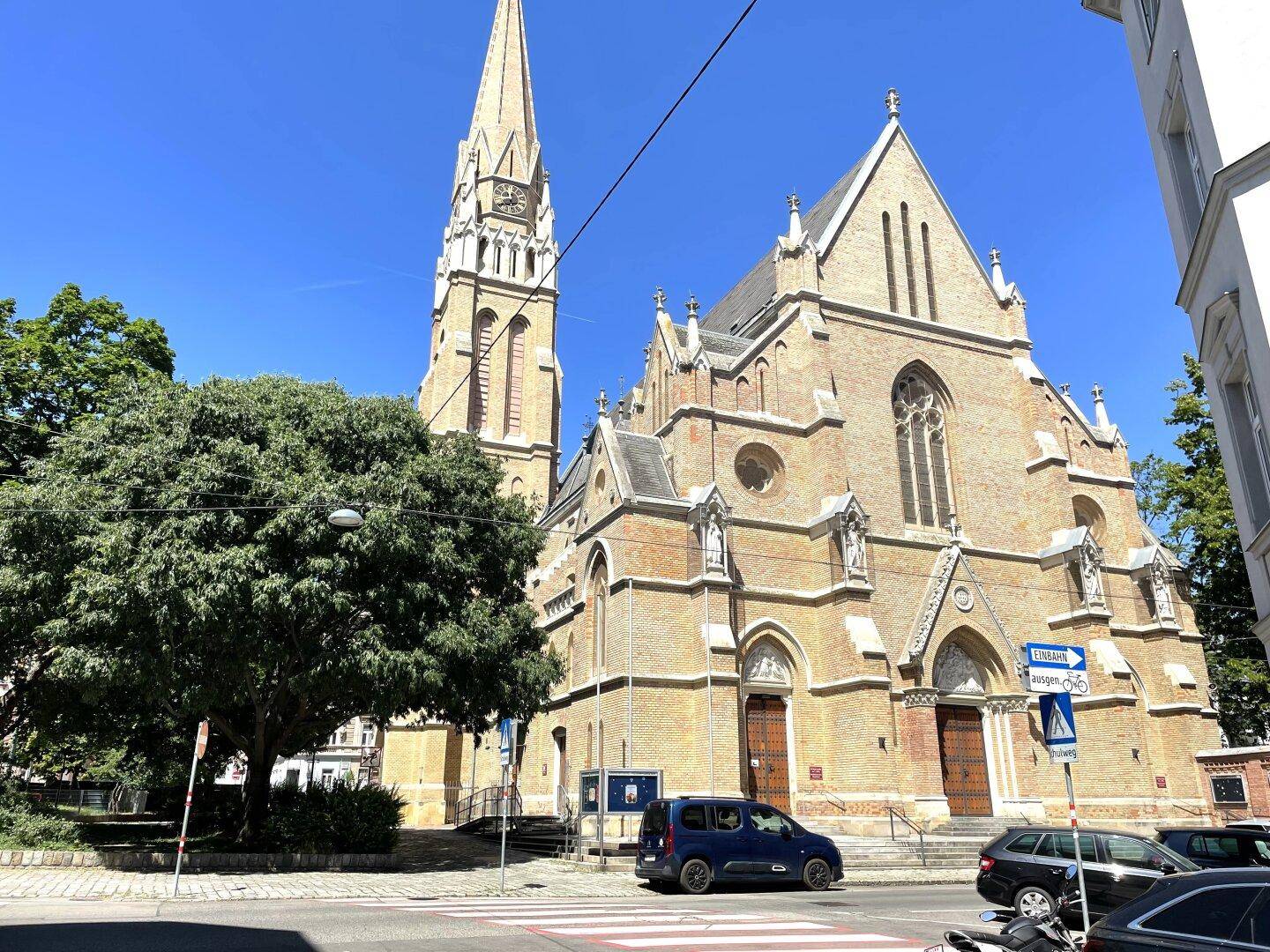 Historische Kirche mit hohem Turm und gotischen Architekturelementen unter blauem Himmel.