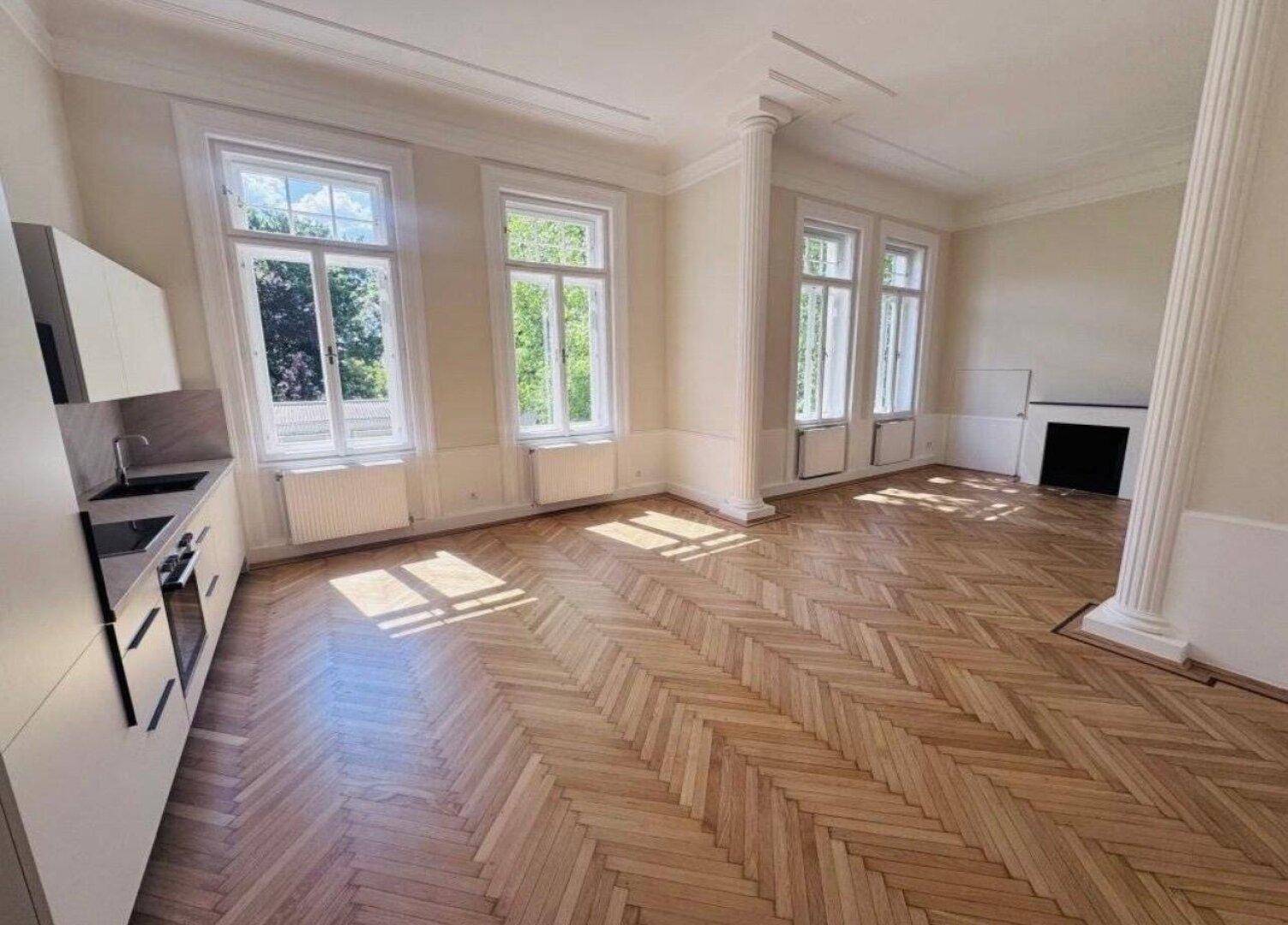 Heller Wohnbereich mit Fischgrätparkett, moderner Küchenzeile und dekorativem Kamin.