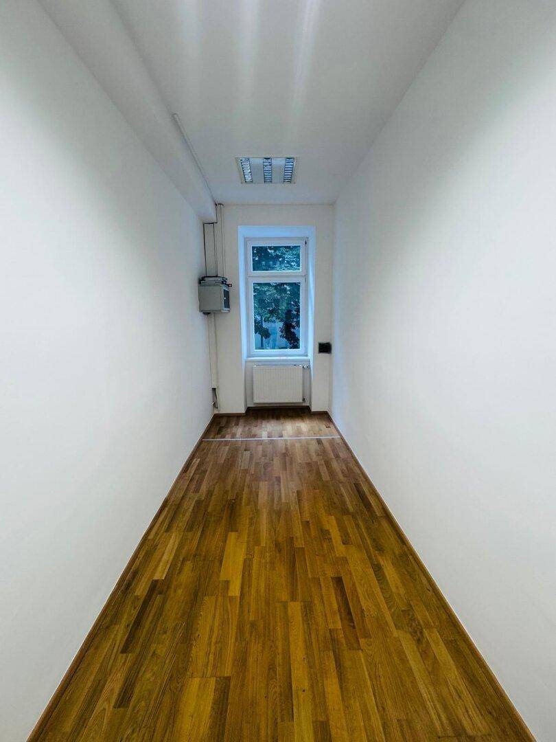 Schmaler, langer Raum mit einem Fenster am Ende und hellem Holzparkettboden.