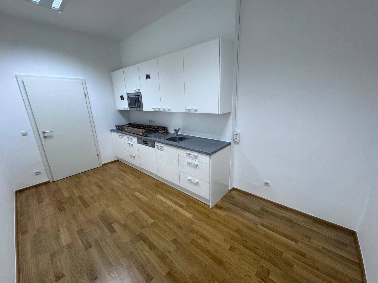 Moderne Küchenzeile mit weißen Schränken, Spüle und integrierten Geräten in einem hellen Raum.
