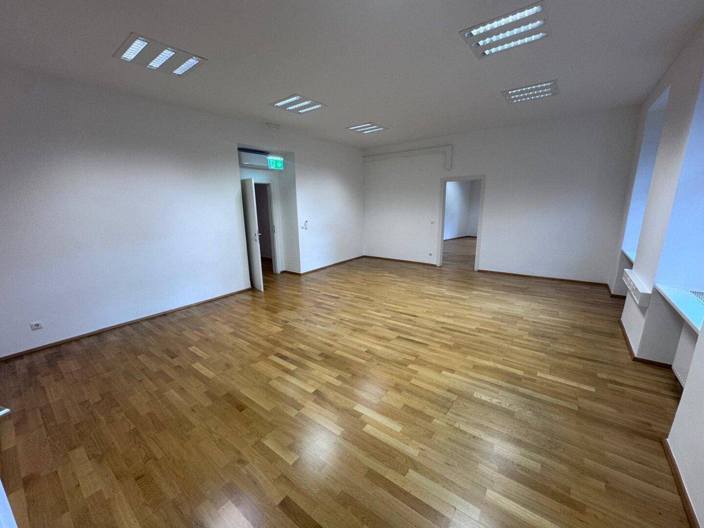 Großer, heller Büroraum mit Holzparkett und mehreren Türen, ideal für flexible Nutzung.
