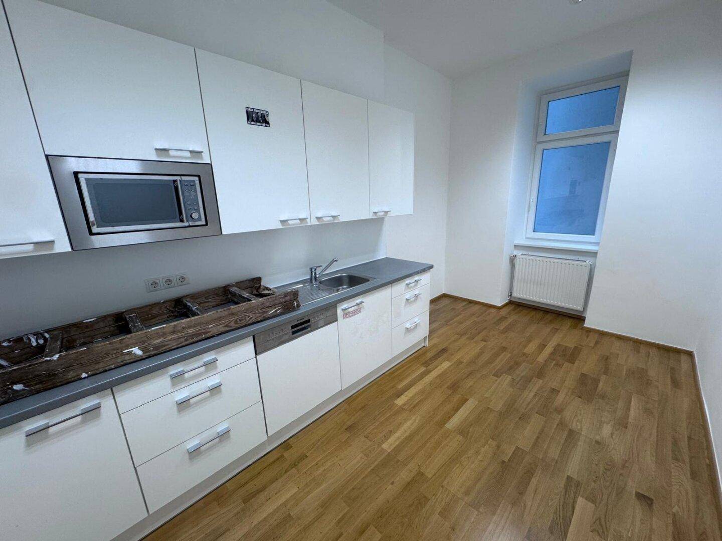Moderne Küchenzeile mit weißen Schränken, Spüle, Mikrowelle und Fensterblick.