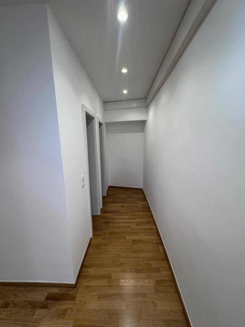Heller Flur mit Holzparkett und Deckenstrahlern, der zu verschiedenen Räumen führt.