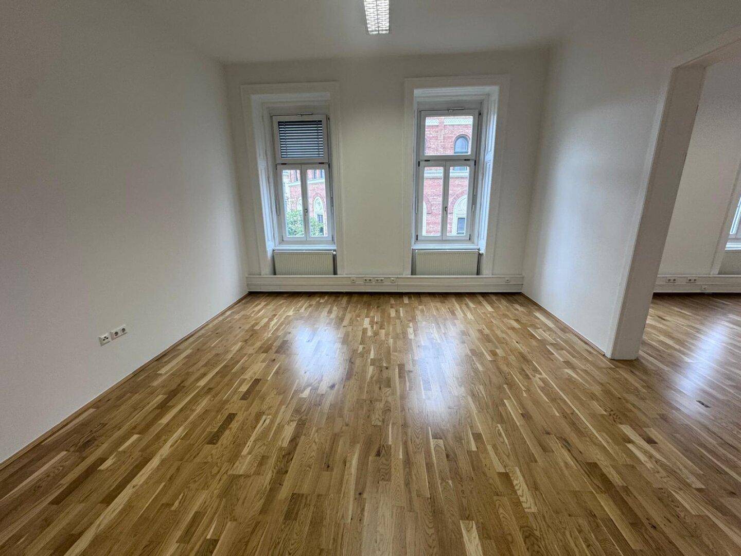 Heller Büroraum mit zwei Fenstern, Holzboden und weißen Wänden, bereit für individuelle Einrichtungskonzepte.