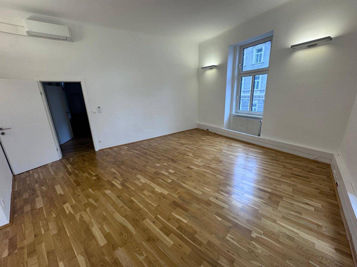 Heller Büroraum mit Holzboden, Klimaanlage und einem Fenster mit Blick nach draußen, sorgt für Komfort.