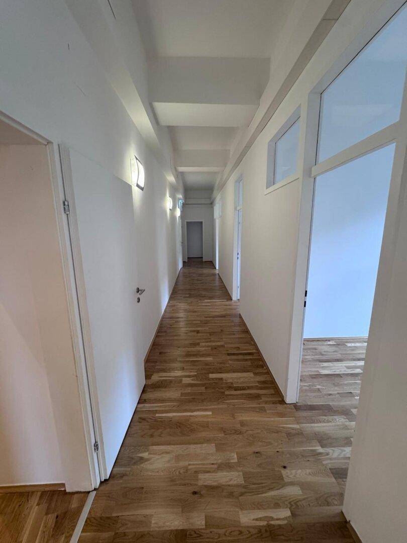 Langer, heller Flur mit Holzboden und Türen zu mehreren Büroräumen, gut beleuchtet und funktional.
