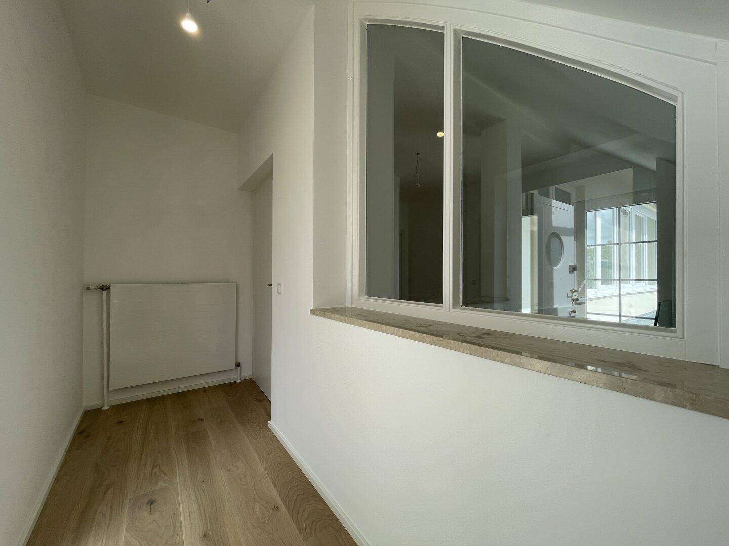Heller Flur mit Holzboden und einem großen Innenfenster, das Licht in den Raum lässt.