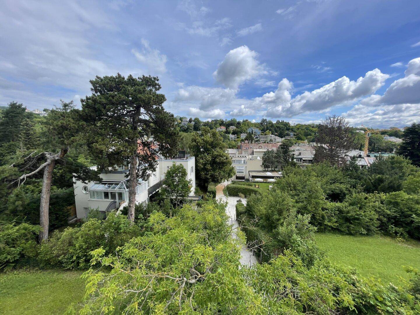 Panoramablick über eine grüne Wohngegend mit vielen Bäumen und Häusern unter blauem Himmel.