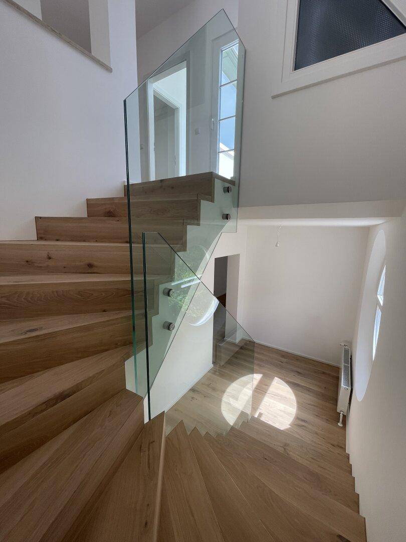 Moderne Holztreppe mit eleganter Glasbrüstung und hellem Holzboden in einem offenen Bereich.