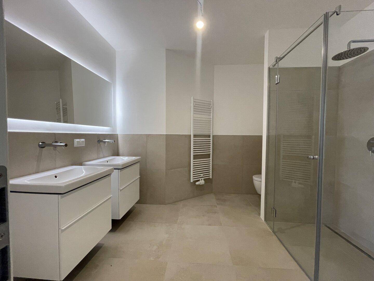 Modernes Badezimmer mit Doppelwaschbecken, begehbarer Dusche und beheiztem Handtuchhalter.