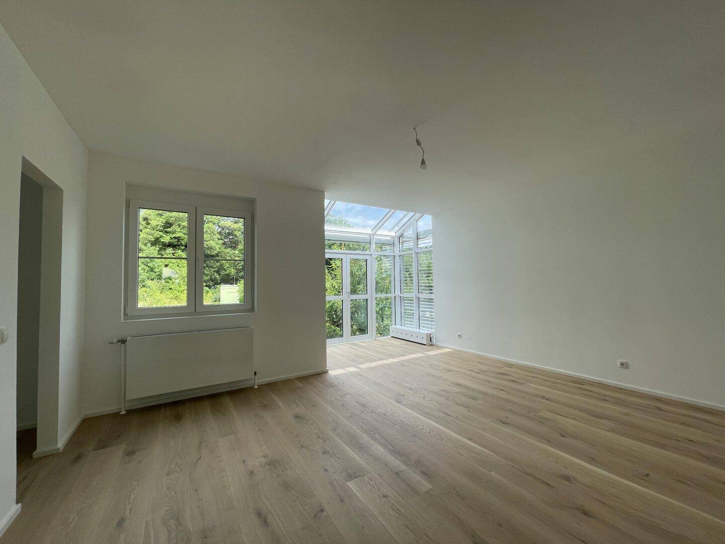 Heller Wohnbereich mit Holzboden und angrenzendem Wintergarten mit viel Tageslicht.