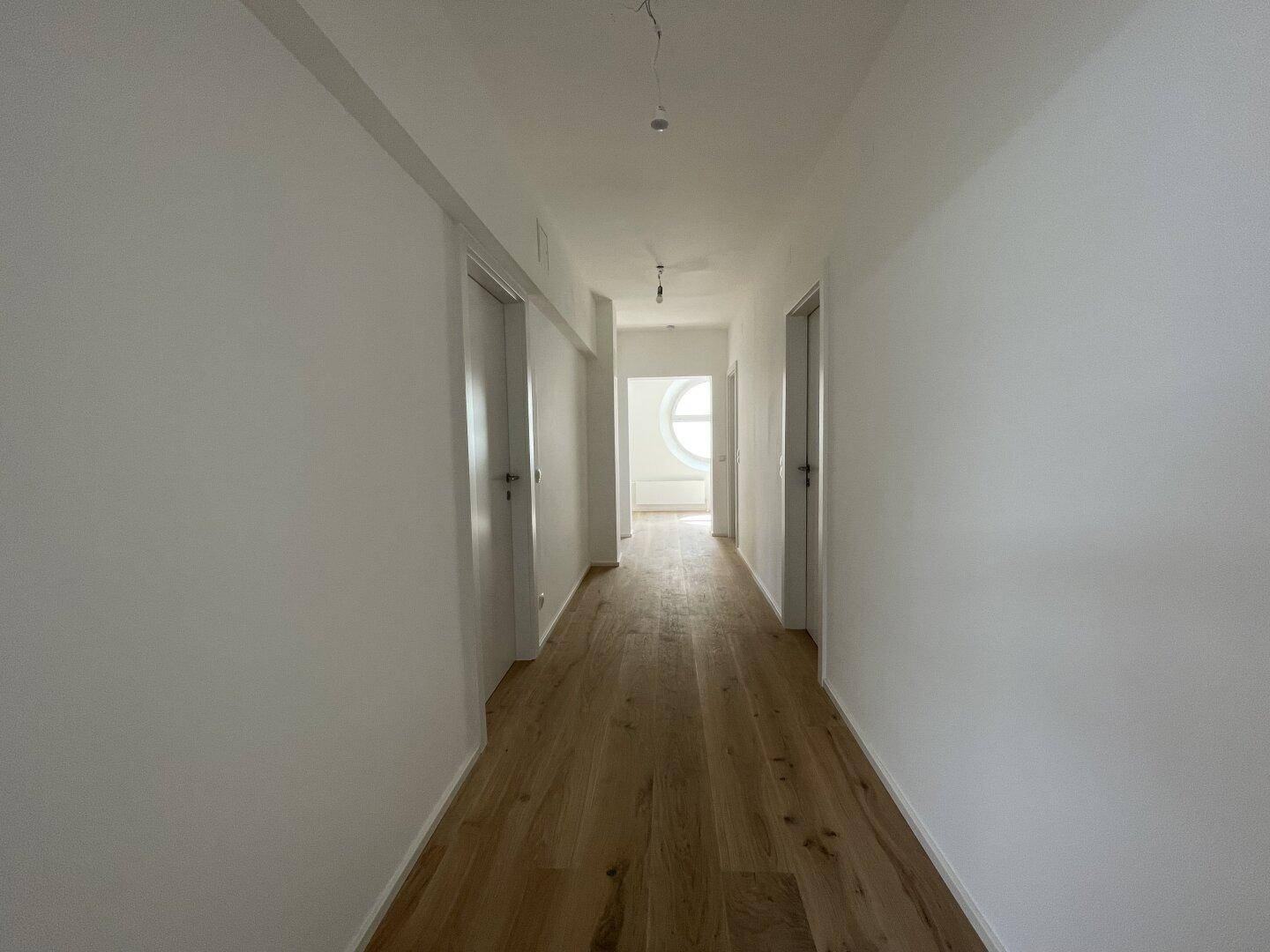 Langer, heller Flur mit Holzboden und Türen, der zu verschiedenen Räumen führt.