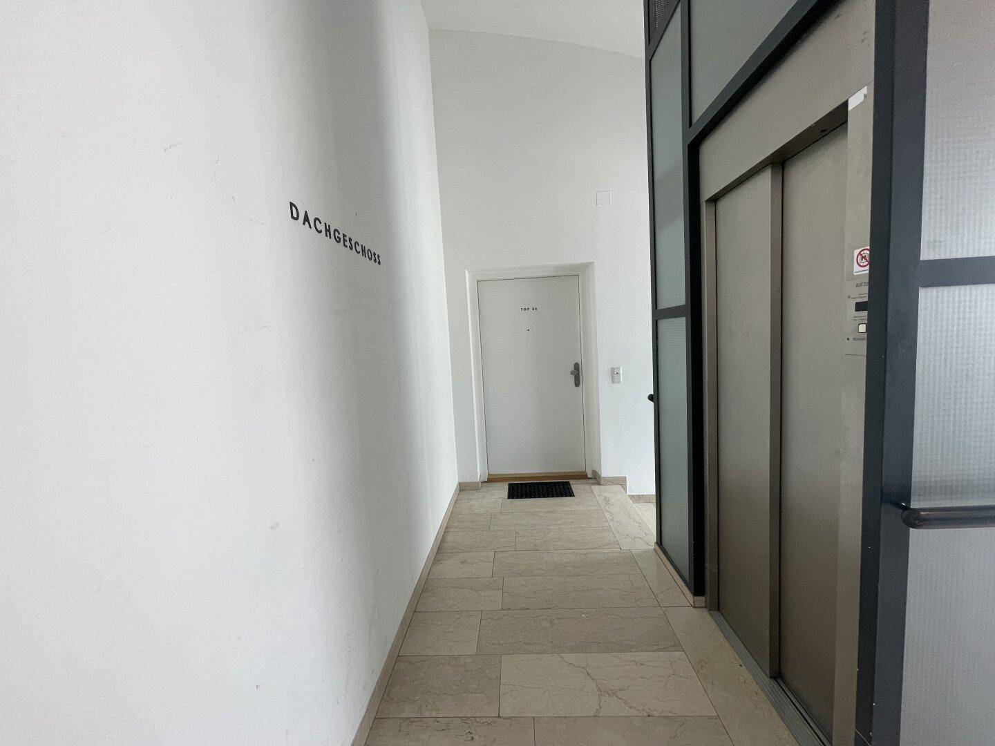 Heller Eingangsbereich mit Aufzug und Fliesenboden, der zum Dachgeschoss führt.