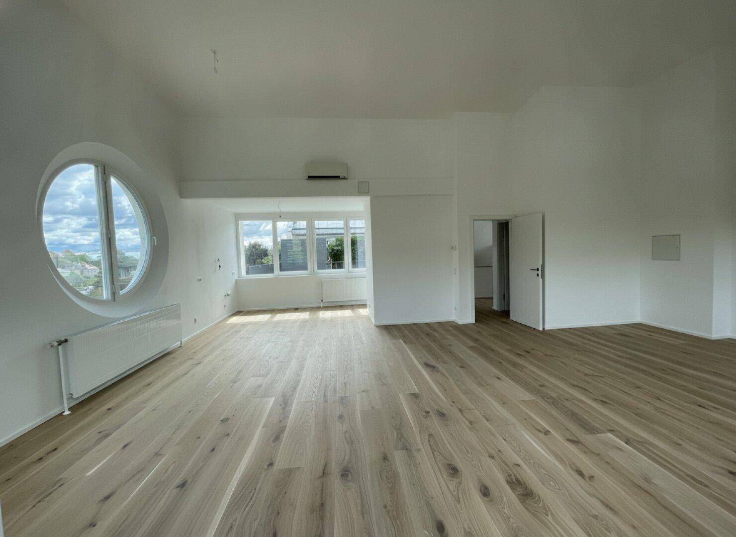 Geräumiges, helles Zimmer mit Holzboden, großen Fenstern und Zugang zu weiteren Räumen.