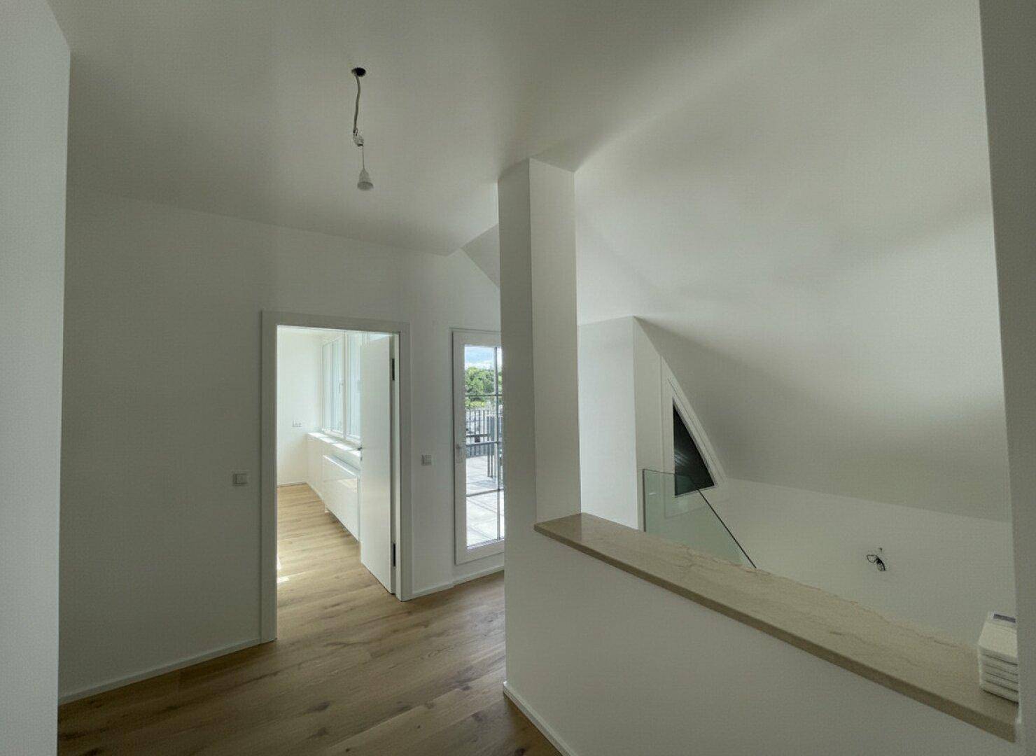 Heller Flur mit Holzboden, schrägen Decken und Zugang zu einem Balkon und weiteren Räumen.