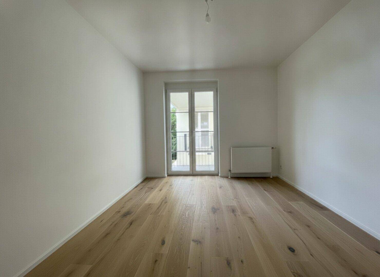 Helles Schlafzimmer mit Holzboden und Zugang zu einem französischen Balkon.