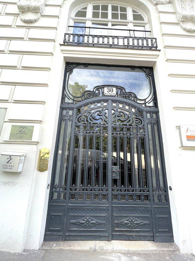 Elegantes, kunstvoll verziertes Eingangstor aus Metall mit der Hausnummer 30 und einem französischen Balkon darüber.
