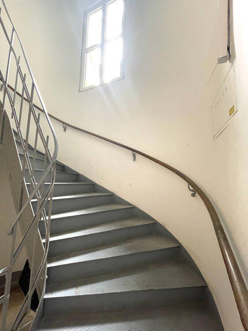 Geschwungene Treppe mit Metallgeländer und Holzhandlauf, beleuchtet durch ein Fenster.