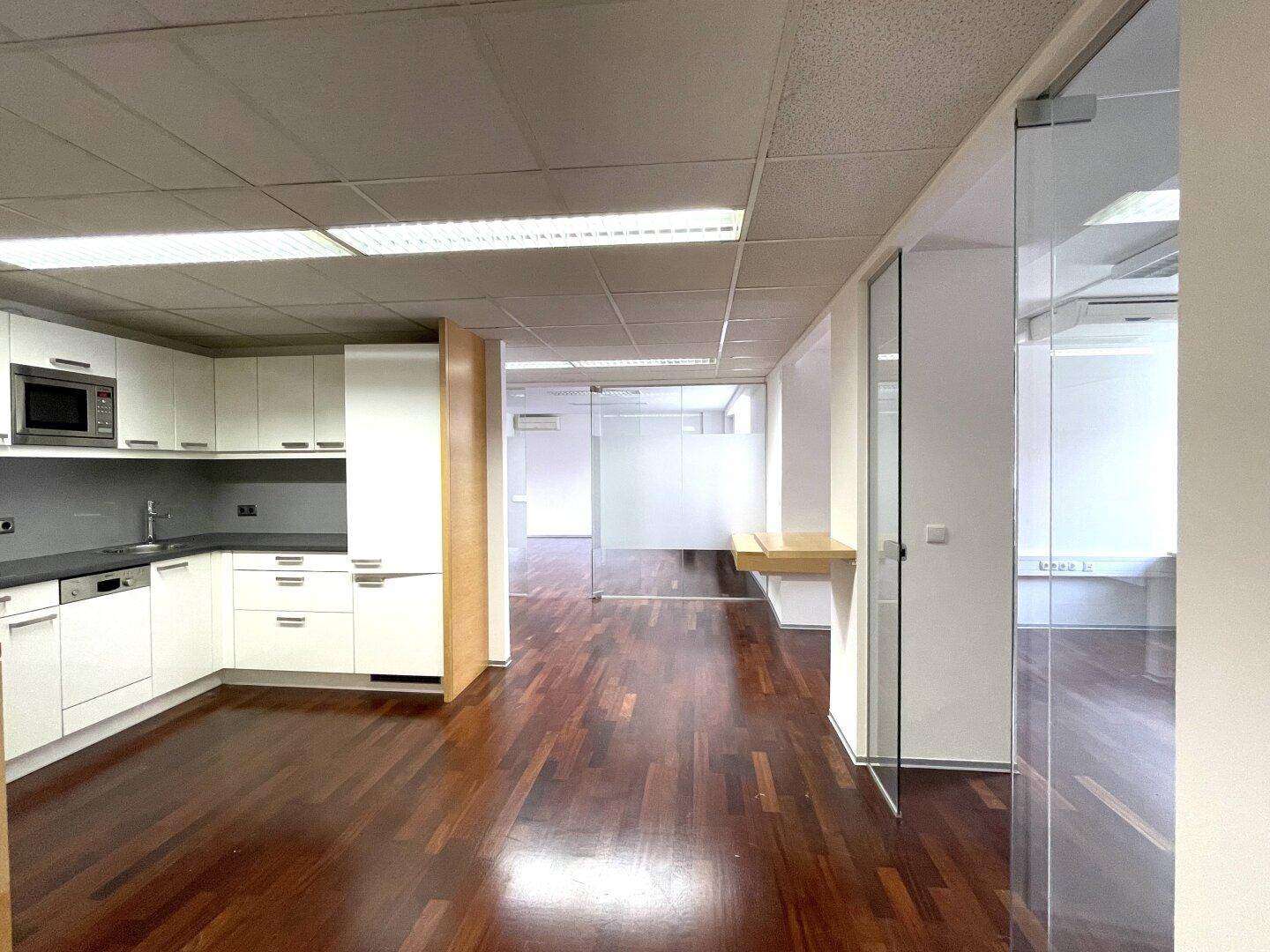 Offener Bürobereich mit moderner Küchenzeile, dunklem Holzboden und Glaswänden.