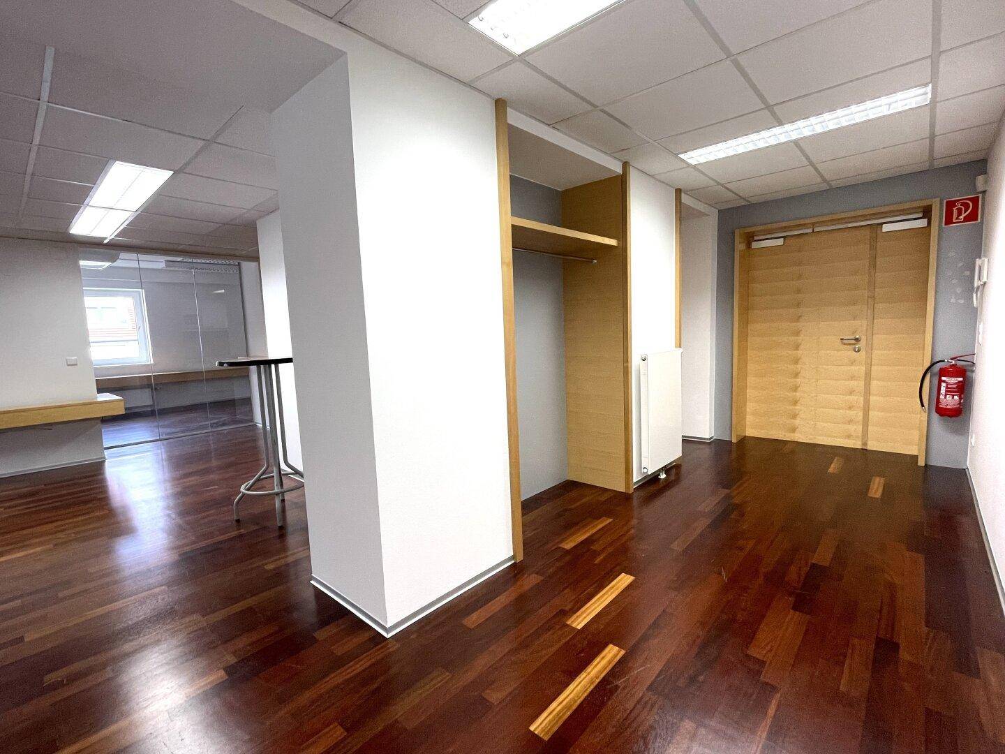 Büroflur mit dunklem Holzboden, Holzeinbauten und einer Brandschutzausrüstung.