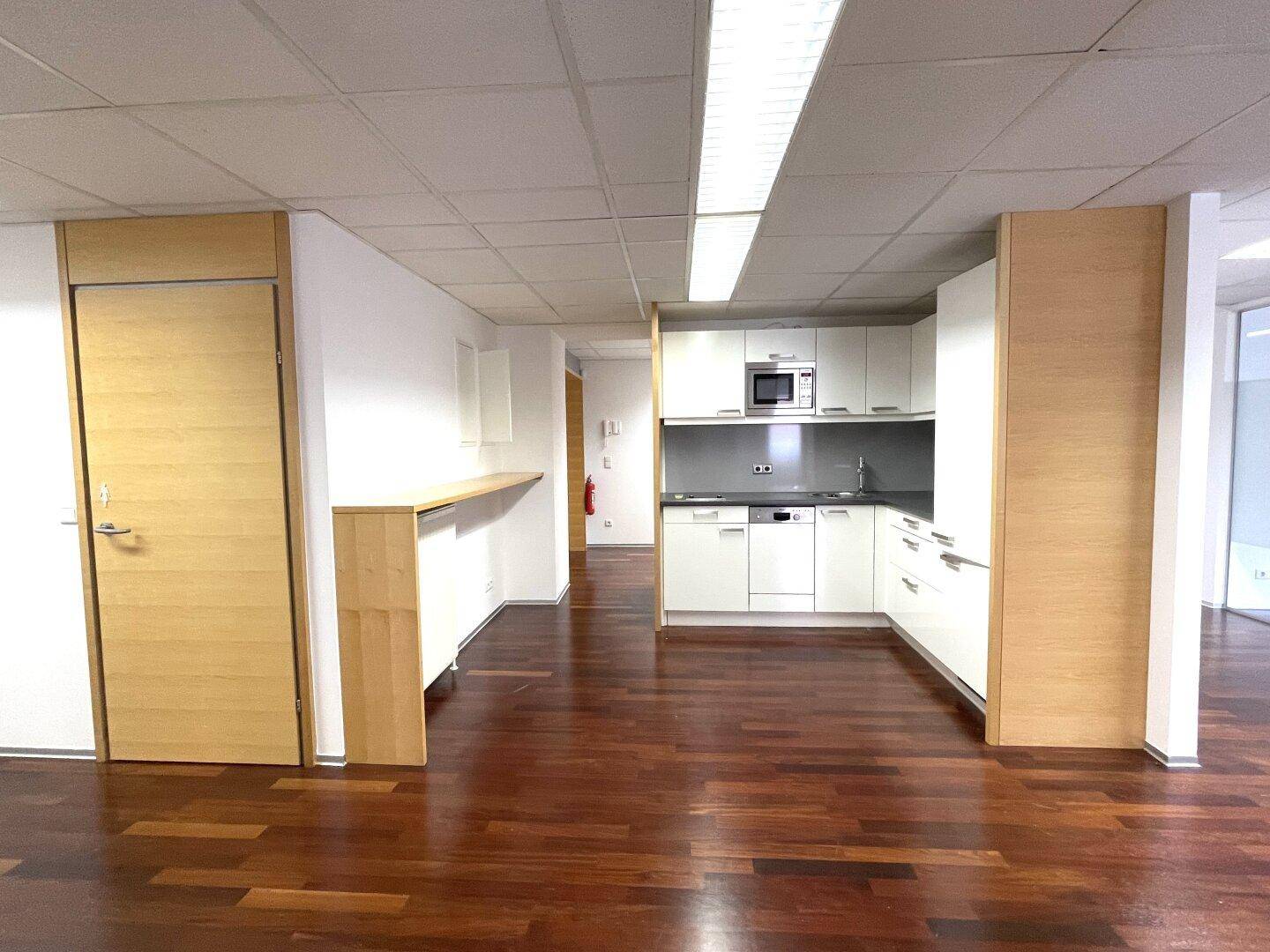 Offener Bürobereich mit integrierter Küchenzeile, Holzboden und Holztüren.