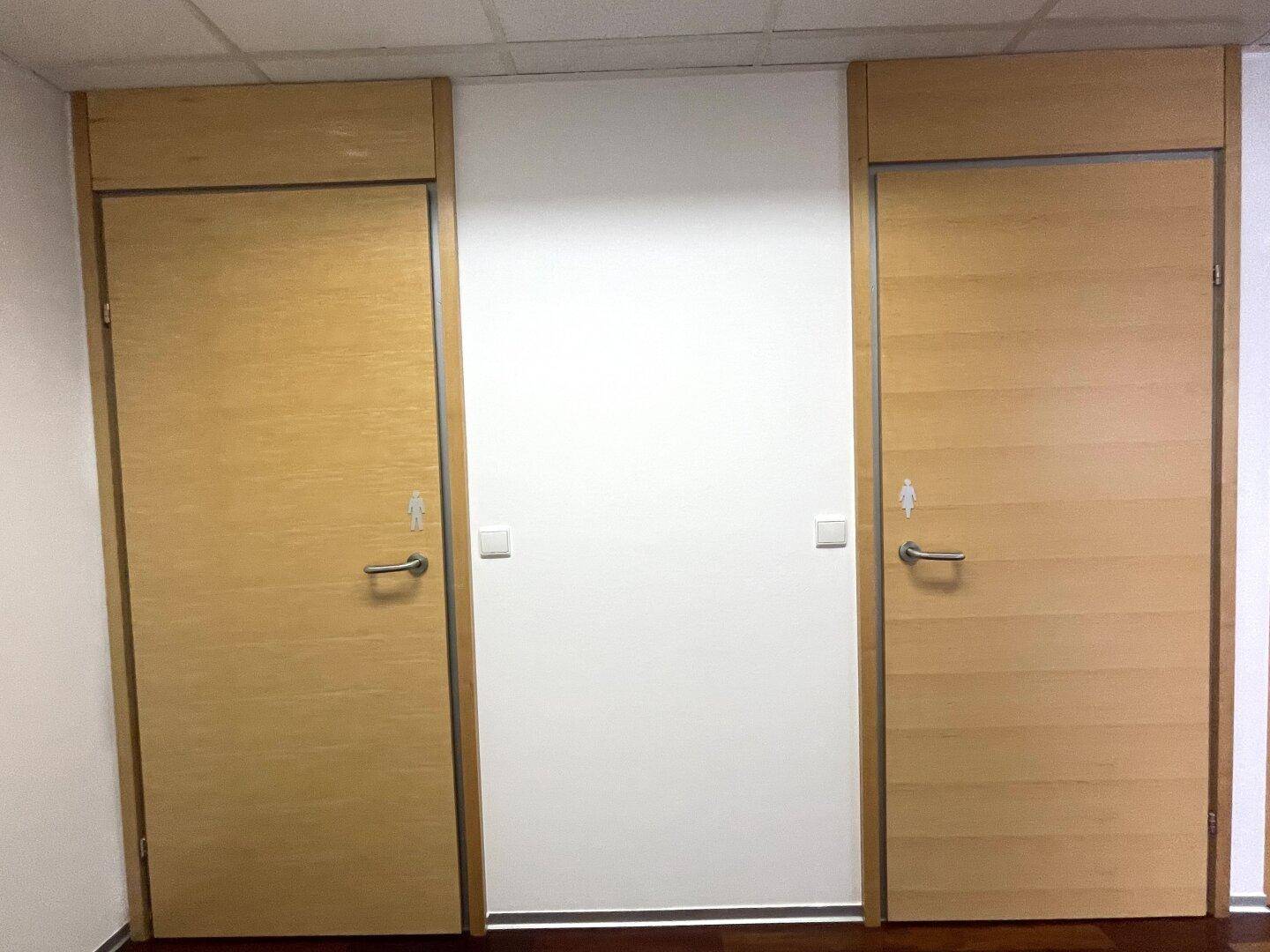Zwei Holztüren zu den Toiletten, gekennzeichnet mit männlichen und weiblichen Symbolen.