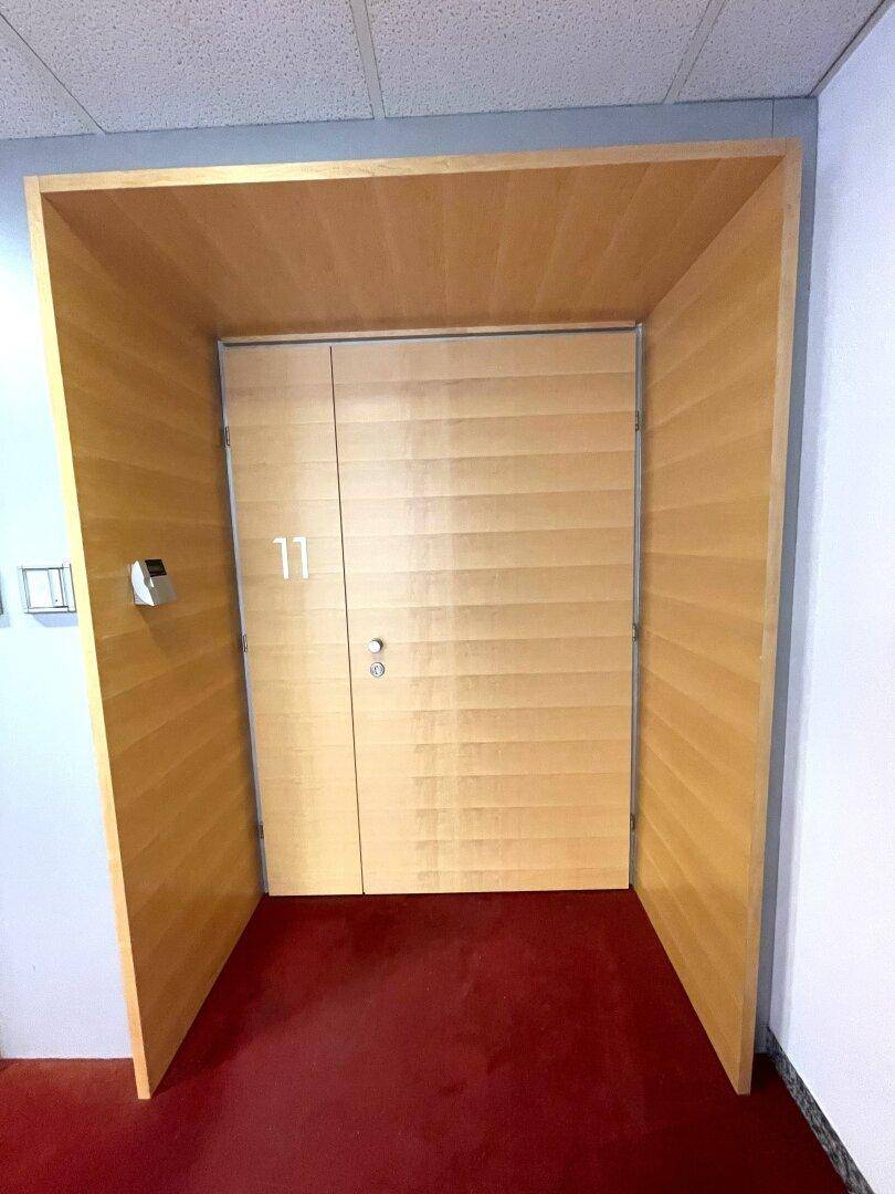 Holztür zu einer Büroeinheit, umrahmt von Holzverkleidungen und rotem Teppichboden.
