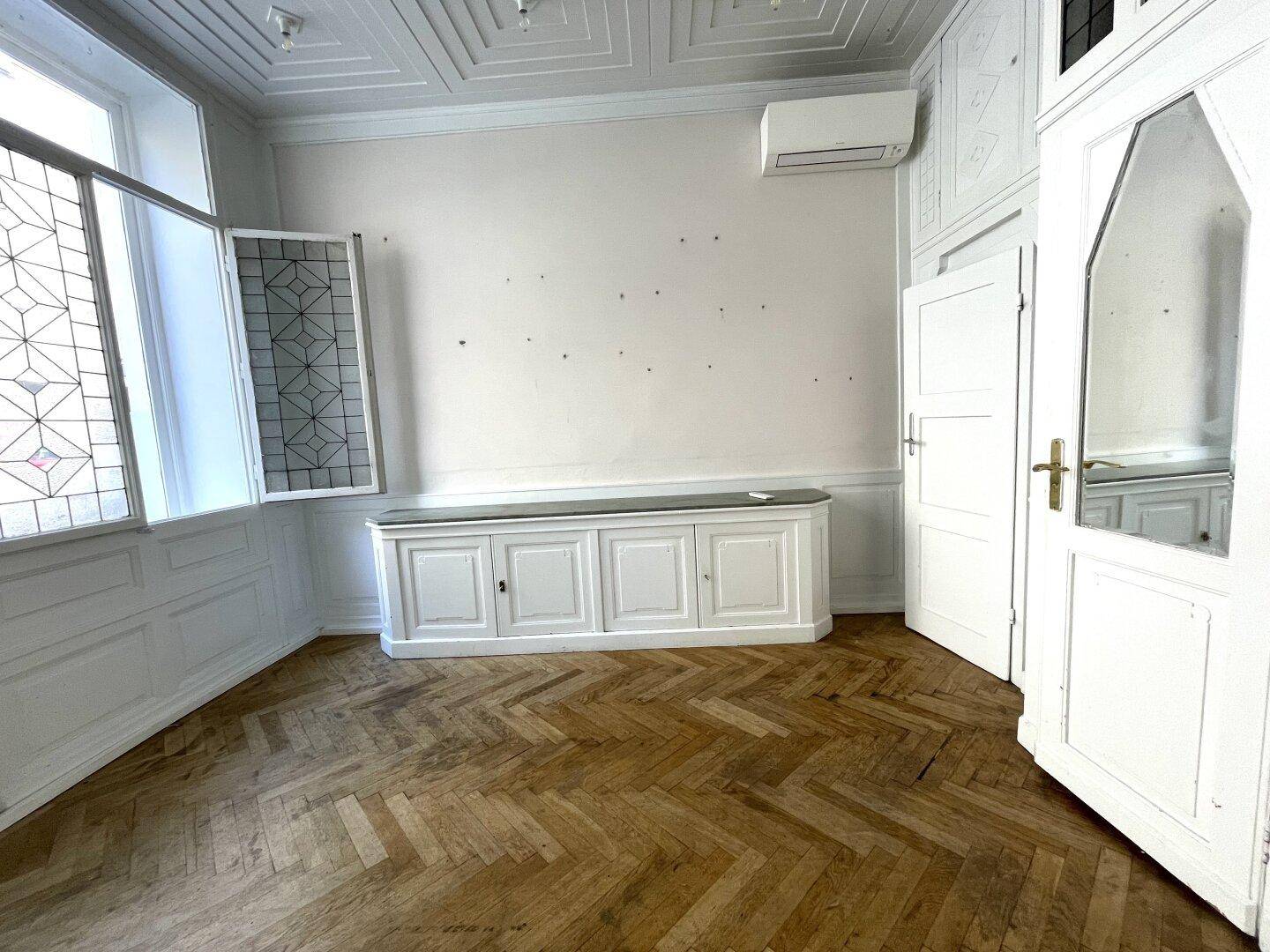Heller Raum mit Klimaanlage, dekorativen Fenstern und eingebauten Schränken.