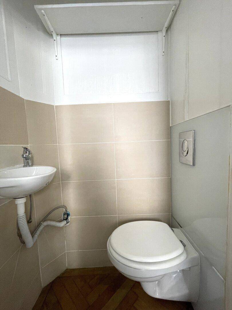 Kompakte Gästetoilette mit Wand-WC, kleinem Waschbecken und hellen Fliesen.