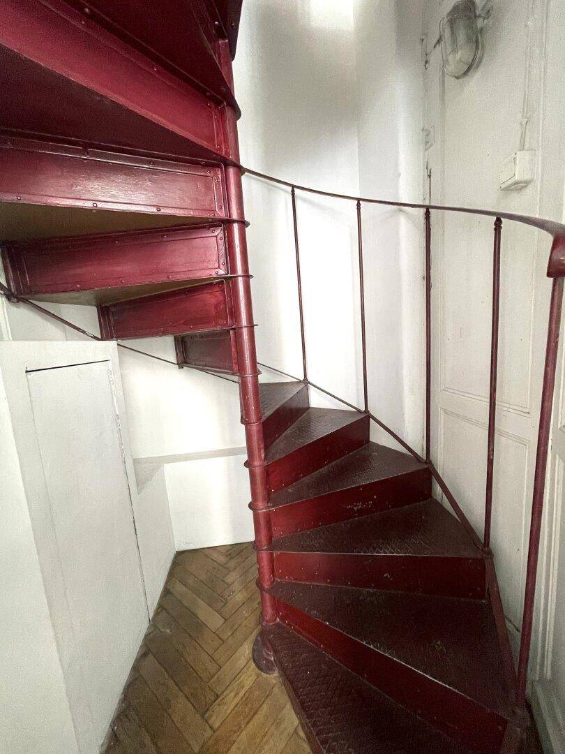 Auffällige rote Wendeltreppe mit schmiedeeisernem Geländer und Fischgrätparkettboden.