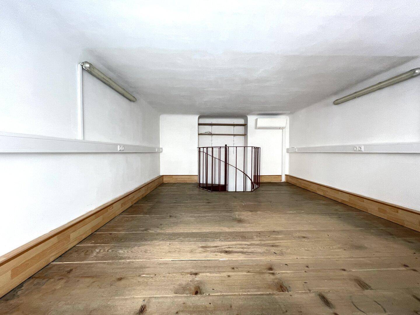 Offener Loftbereich mit Holzdielenboden, weißen Wänden und niedriger Decke.